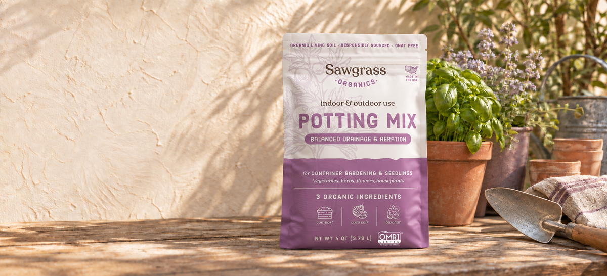 Front-facing Sawgrass Organics Potting Mix bag on a clean garden bench beside basil and purple flowers